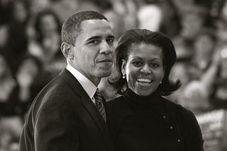 Black & White Photo of President Barack Obama and First Lady Michelle Obama standing next to each other, looking back at the camera