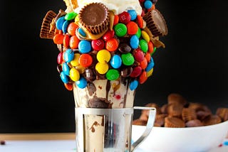 A colourful milkshake full of M&Ms and chocolates along with whipped cream and thick chocolate ice cream.