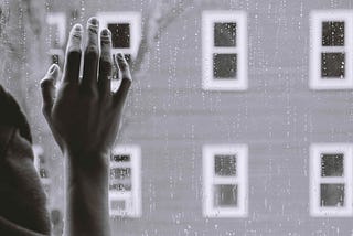 Hand on window, looking out over a rainy day, grayscale