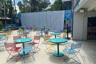 Picture of Dodger Stadium where the mural with Julio Urias has been covered with a white tarp. Colorful chairs and tables are in the foreground.