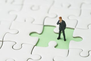 Image of a jigsaw puzzle with one piece missing and a man standing in the space of the missing piece