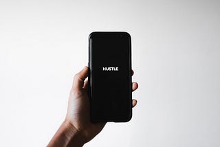 Smartphone displaying the word Hustle on a black screen.