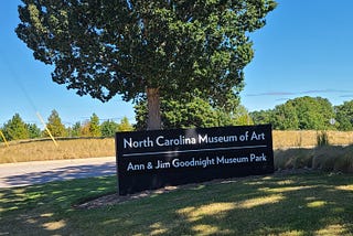 A sign that says ‘North Carolina Musuem of Art’ in front of a tree