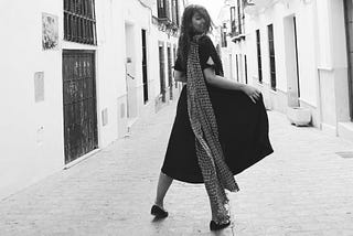 Woman standing in street with long dress and scarf blowing in the wind