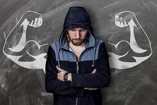 man reflecting with his arms crossed having behind him a drawing of muscular biceps that represent our ego