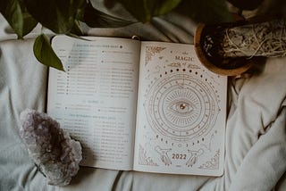 A journal which says ‘the magic of 2022’ and includes astrological events. It’s surrounded by an amethyst crystal and sage for smudging.