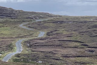 a long, winding single track road over deserted heath with the sea in the distance