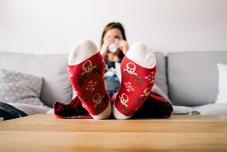 Woman sitting on couch drinking hot chocolate while wearing Christmas socks