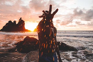 Guy in the sunset at a beach, splashing water at a camera.