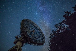 Large radio telescope set against a night sky full of stars, with the Milky Way galaxy visible in the background