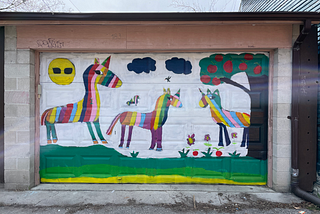 Colourful garage door in one of Toronto’s laneways features a painting of 3 rainbow horses lounging on a field with a sun wearing sunglasses.
