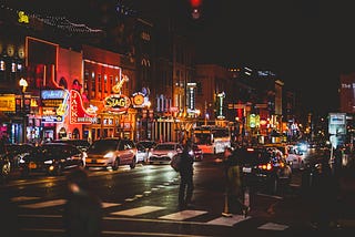 A busy strip at night, lit up with signs from bars and cars in the street.