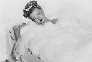 A black and white photo of a woman asleep in a bubble bath