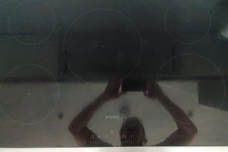 Overhead image of a induction hob. The surface is reflective black and shows the faint marking for five rings and the control dials to regulate the cooking rings.