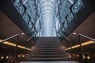 Stone stairs with railing on either side. Vaulted glass ceiling above stairs.