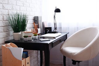 The visual showcases a small home office environment with some plants, computer, chair and file organizer.
