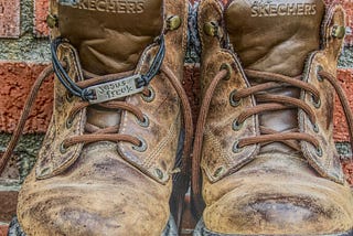 This image shows a pair of brown hiking boots with a silver tag that says “Jesus Freak” tied to the laces. This photograph is © Copyright 2010–2023 to Deb Wax, the photographer. All Rights Reserved.