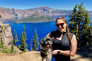 Deanna with her dog on a cliff overlooking a lake and mountains.