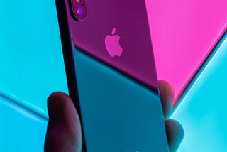 Photo of someone holding an iPhone against a neon background, taken by Daniel Korpai on Unsplash.