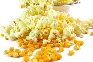 Popcorn and kernels spill from a white cereal bowl