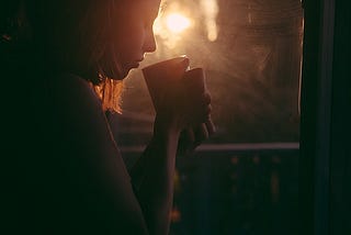 Girl drinking tea in the sem-darkness in front of a window with a light shining through it