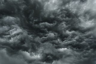 Menacing storm clouds swirl in this photo, most a dark greenish gray color with few light spots.