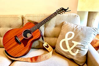 Picture of guitar and a pillow with an ampersand sitting on a couch