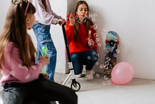 Young girls on a scooter blowing bubbles