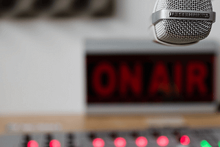 Radio broadcaster’s desk. Mixing board, mic, and “on-air” sign like the old days.