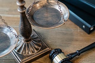 Close-up photo of a scale of justice, a gavel, and books on a wooden surface.