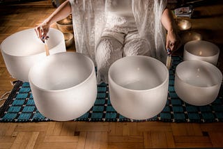 A woman sitting on a mat playing crystal singing bowls