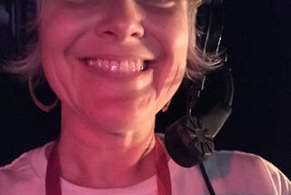 A selfie backstage at a theater of a stage manager on headset. She smiles and wears a white t-shirt.