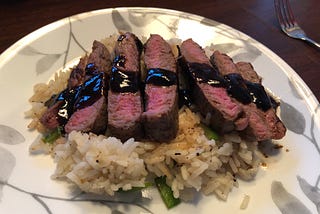 steak slices arranged on a bed of rice with tamari sauce drizzled on top