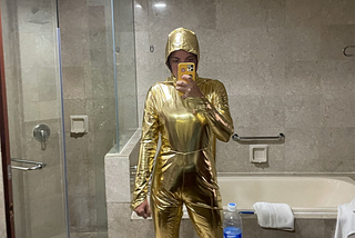 The author takes a mirror selfie wearing an all gold jumpsuit, dressed to look like an Oscar award