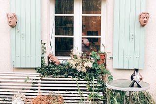 Open shutters on a window with flower box and slatted bench below