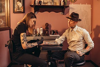 A Stick-and-Poke artist performing this technique on a well dressed customer.