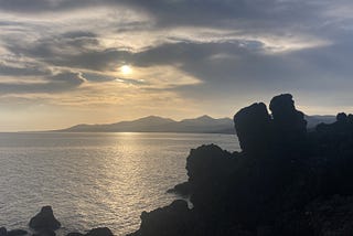 A slightly hazy late afternoon sky looking west over the sea towards Papagayo, the mountains to the south of Lanzarote, from Puerto del Carmen, with black volcanic rocks in the foreground.
