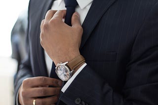 A business man setting his tie, wearing a brown wrist watch