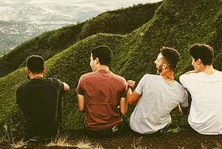 Four young men seated atop a mountain, overlooking a city.