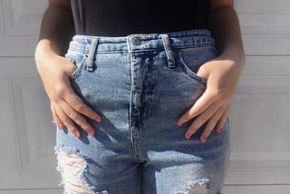 Light blue high-waisted jeans with a few holes in them. Hands in pockets in the front.