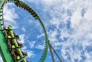 Green rollercoaster against a blue sky and clouds.