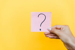 Cropped view of woman holding sticky note with question mark on orange