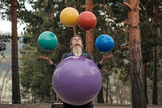 A juggler juggling four normal and one huge ball