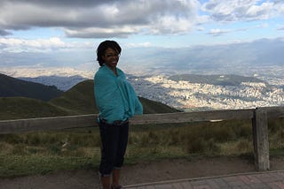 Aneisha standing in front of a mountain in Ecuador wearing a blue shawl.