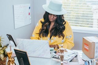 Woman wearing a hat writing at a laptop.