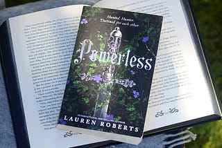 Front of the book Powerless by Lauren Roberts, on top of an open book