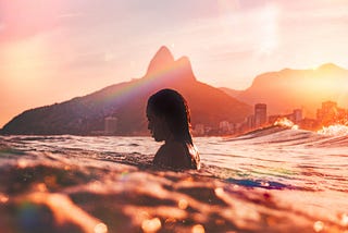 an image of a woman swimming alone in the ocean looking into the water, contemplatively.