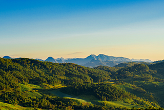 Photo of a green mountain range against a blue, cloudless sky.