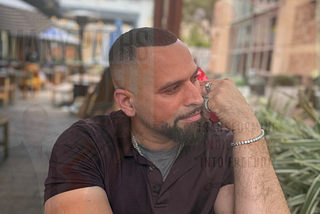 International best sellling author christopher knight lopez sitting in a park with a phone to his ear looking away from the camera.