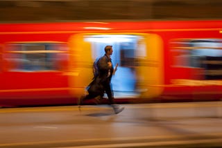 A man runs past a bright orange train to catch a train at Paddington station.